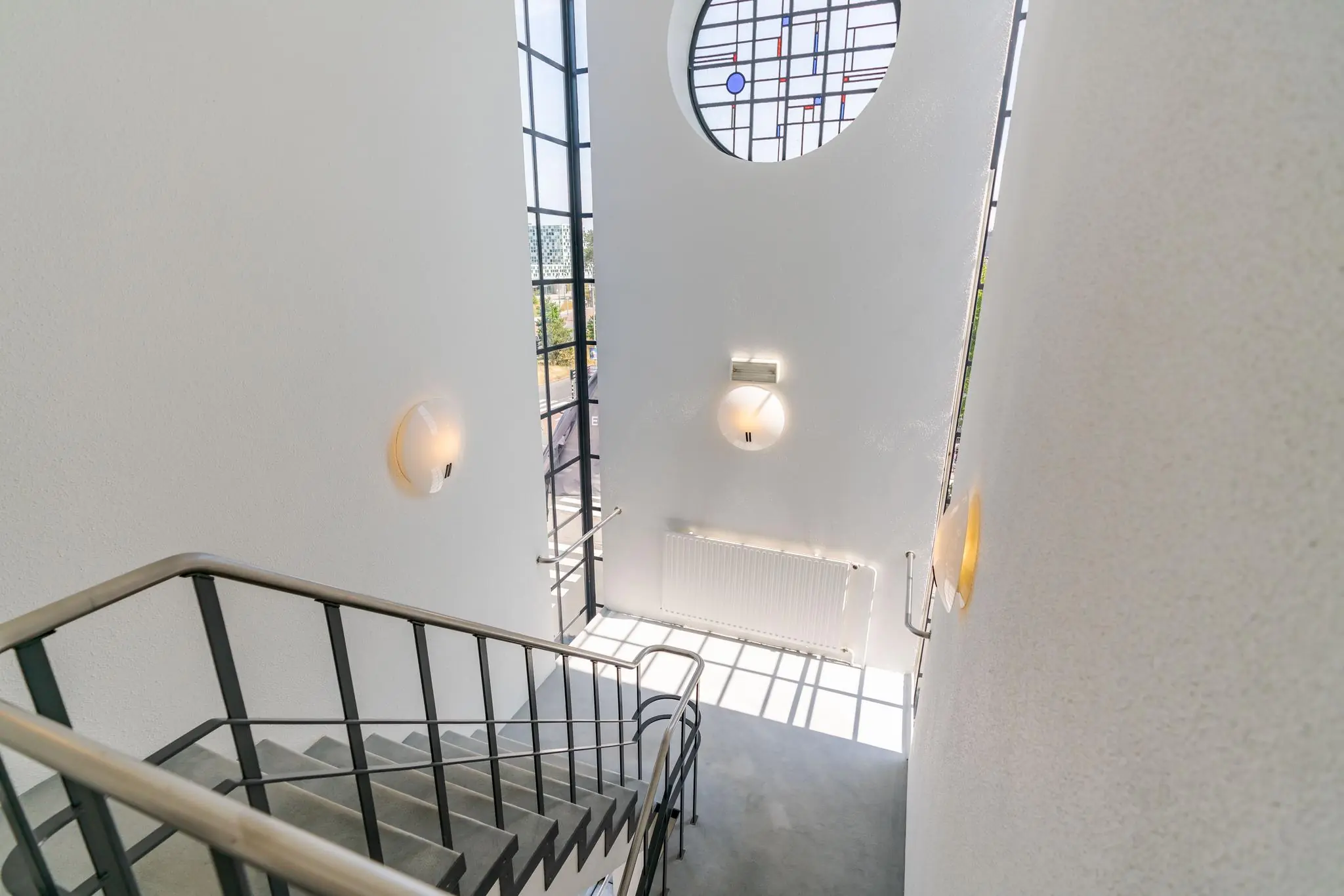 Licht trappenhuis aan de Van Alkemadelaan met modern glas-in-loodraam en strakke stalen leuning.